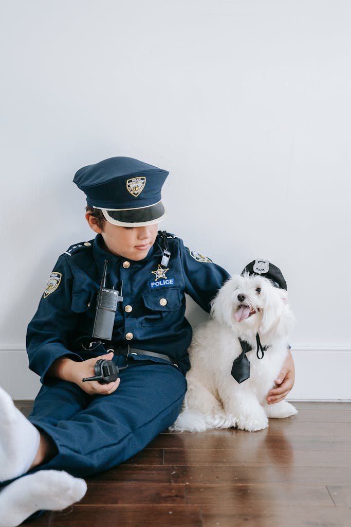 Adorable child and dog in police costumes sitting on a wooden floor against a white background.